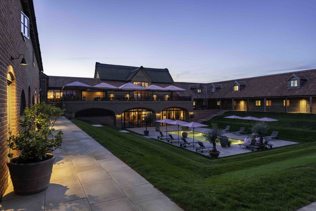Estate courtyard at dusk with lit pool, parasols and brick barn buildings